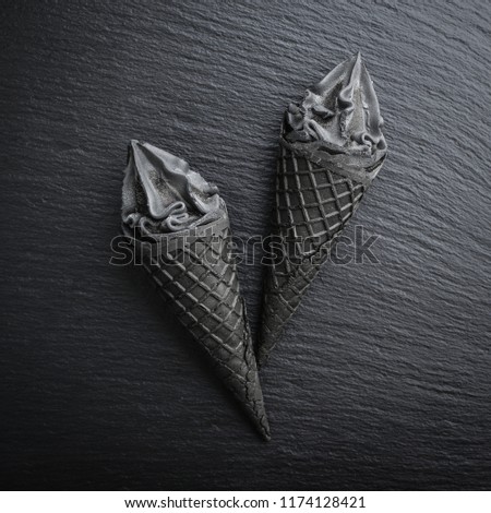 Black ice cream in cone on black slate background, top view