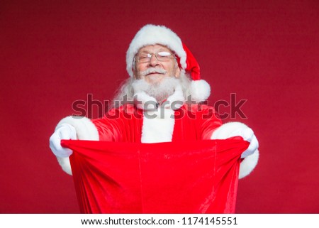 Christmas. Santa Claus in white gloves opened the bag with gifts and looks into it. Offers to take the gifts. Isolated on red background.