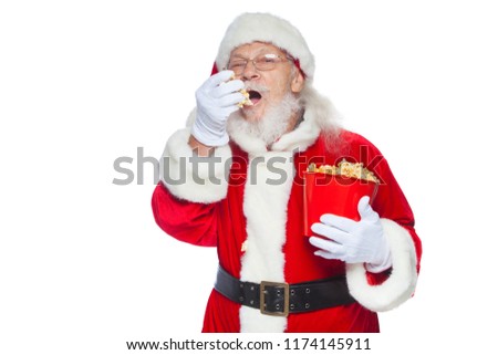 Christmas. Smiling, kind Santa Claus in white gloves with his mouth open holds a red bucket with popcorn with one hand, takes some popcorn and prepares to eat it with the second hand. The concept of
