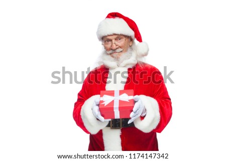 Christmas. Smiling Santa Claus in white gloves is holding a gift red box with a bow. Pointing at the gift. Isolated on white background.