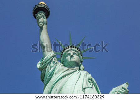 Looking up at the face and torch of the Statue of Liberty, against a clear blue sky