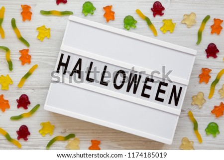 'Halloween' word on modern board, jelly monsters and worms over white wooden background, overhead view. From above, top view.