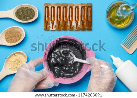 Photo from above with pink cup with black clay, mask oil, wooden spoons, comb, human hands with spoon