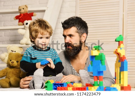 Father and son with smiling faces create colorful constructions with toy bricks. Dad and kid with toys on background build of plastic blocks. Man and boy play together. Family and childhood concept
