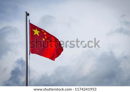 The Chinese flag flutters against the cloudy sky. Clouds are gathering, political problems, conflict. Bottom view, copy space, vignetting.
