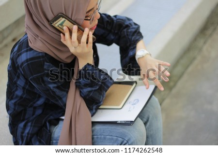 Young beautiful Asian girl wearing hijab on the phone discuss on an assignment for next class. education concept.