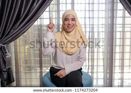 A young female businesswoman wearing hijab smiling happily while showing idea hand gesture