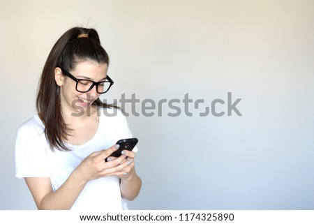Smiling lovely young woman standing and using cell phone over grey background