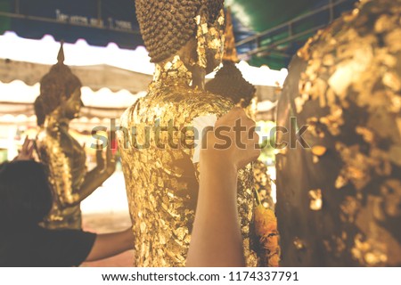 The people put their hands to close the gold leaf where the Buddha statue with many gold leaves buddha statue.