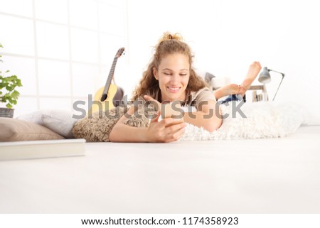 smiling Beautiful young woman using a smart phone lying on living room wooden floor in comfortable home 