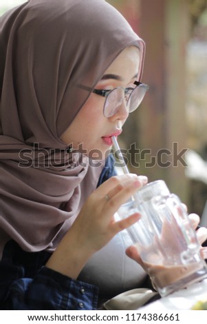 cute Asian hijab girl at café in the morning having breakfast while looking at the pictures in the cameras