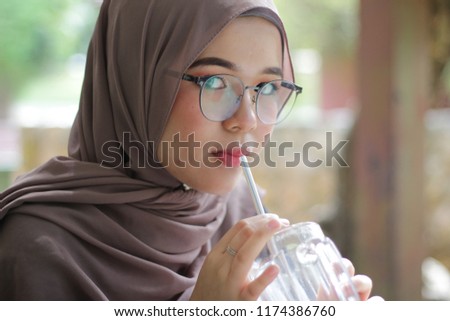 cute Asian hijab girl at café in the morning having breakfast while looking at the pictures in the cameras Royalty-Free Stock Photo #1174386760