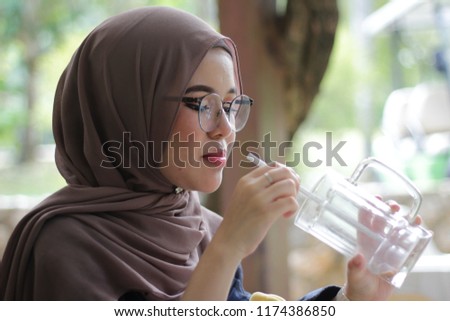 cute Asian hijab girl at café in the morning having breakfast while looking at the pictures in the cameras