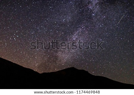 Beautiful and colorful milky way galaxy with meteors in the sky full of stars and dark mountain at foreground.