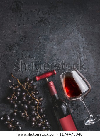Red wine bottle with vintage corkscrew, glass and grapes on retro black background, top view. 
