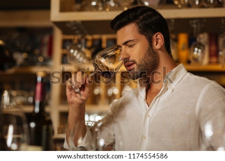 Wine lover. Joyful handsome man trying the taste of wine while choosing what to drink