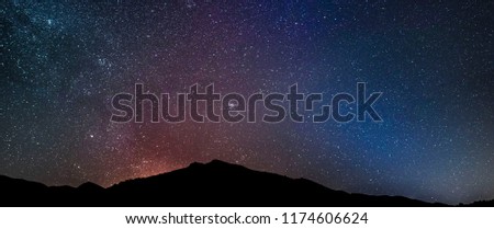 Super colorful panoramic landscape of night sky with dark mountains at foreground.