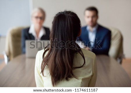 Businesswoman and businessman HR manager interviewing woman. Candidate female sitting her back to camera, focus on her, close up rear view, interviewers on background. Human resources, hiring concept Royalty-Free Stock Photo #1174611187