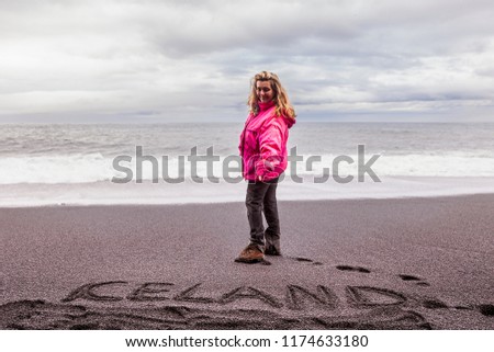 beautiful blonde tourist on the black beach of Vik while pointing to the written Iceland