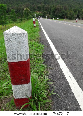 Curved pole is red, white, by the road.