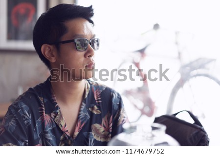 A hipster boy with sunglasses is drinking hot coffee in a loft cafe.