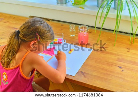 Little girl painting simple picture. Cute girl painting with watercolors. Window background. Selective focus and small DOF.