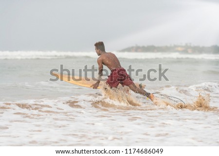 Young dark, handsome, athletic local Native Islander wearing board shorts, jumping on his board to catch a wave to surf