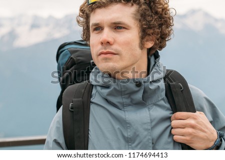 serious adventurous guy with blue eyes looking aside. close up shot. wonderful scenery on the background of the photo