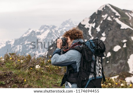 close up back view photo of a young photographer with rucksack taking photos on the top of the mountain. hobby, free time