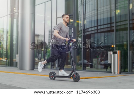 Attractive man riding a kick scooter at cityscape background. Royalty-Free Stock Photo #1174696303
