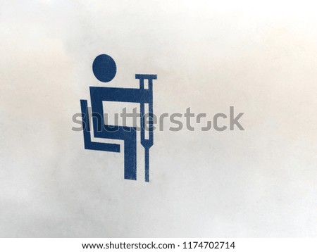 old blue sign of a disabled person with crutches in transport. Badge of movement of the disabled, attached to the white wall