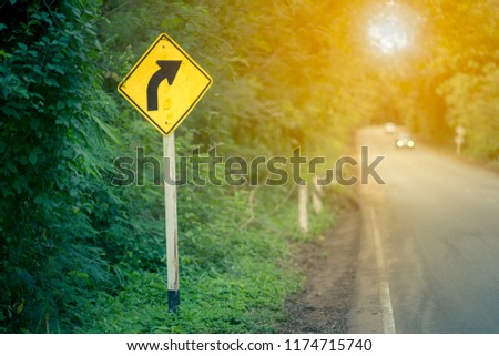 Curve sign traffic, sign black arrow on yellow background show remind for drive car on street. It traffic symbol on roadside on light sun in forest on mountain. Travel must be careful in driving. 