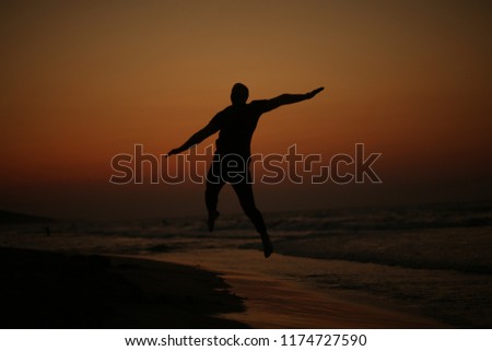Young man with his arms in the air looking out into the beautiful sunset.