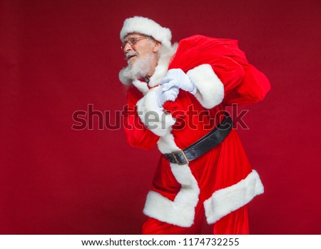 Christmas. Kind and tired Santa Claus in white gloves carries a red bag with gifts over his shoulder. Isolated on red background.
