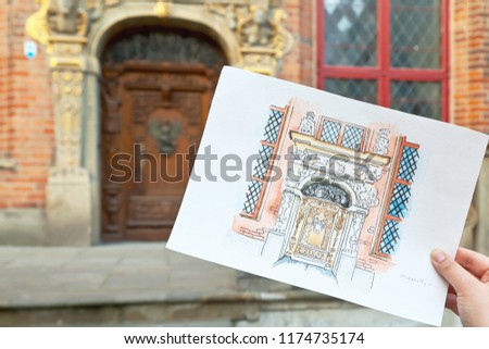 Watercolor drawing in hand against the backdrop of the old city. Gdansk, Poland. Old wooden door.