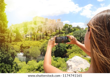 Cute young woman takes a picture of the Acropolis, Athens, Greece. Famous ancient Greek Acropolis is the main landmarks of Athens. Female tourist visits the Athens and takes a photo.