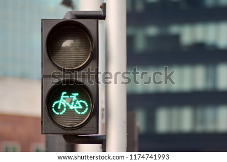 Bicycle traffic light with bicycle icon and active green resolving light on the background of summer city