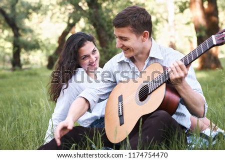 young couple sitting in the forest and playing guitar, summer nature, bright sunlight, shadows and green leaves, romantic feelings