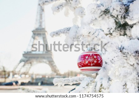Christmas tree covered with snow and decorated with red ball on a street of Paris, France. Eiffel tower in the background. Trip to France during holidays season concept