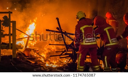 Firemen at work in uniform in from of the fire putting the rests of a burning falla sculpture made of paper at Las Fallas festival in Cullera, Valencia, Spain.