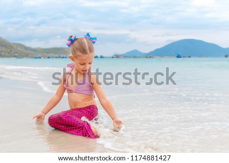 Little beautiful girl dressed in swimsuit as a mermaid sits on the seashore