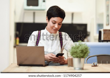 Young woman with very short haircut looking at her smart phone. Businesswoman working at home concept.