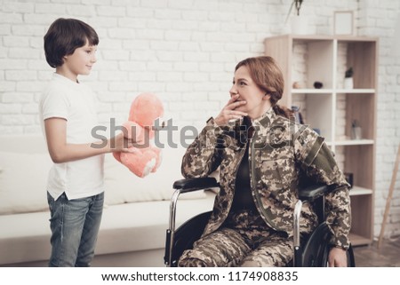 Woman Veteran In Wheelchair Homecoming Concept. Family Meeting. Leaving From War. Fluffy Toy. Camouflage Uniform. Son Hanging. Feelings Showing. Patriotic Comeback. Paralyzed Soldier.