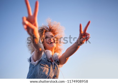 Young stylish woman with very lush hair show victory sign. Young woman with big headphones. outdoors portrait of a trendy girl