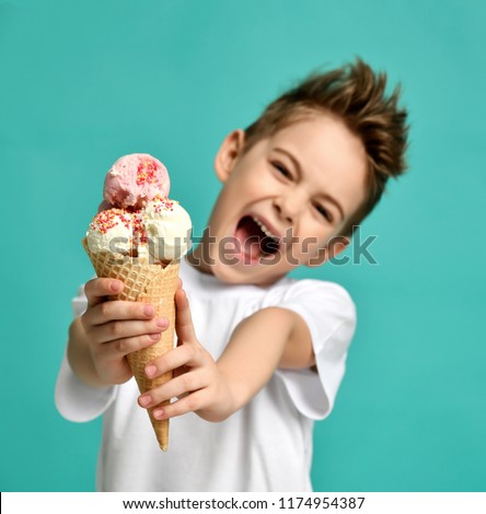 Baby boy kid hold strawberry vanilla ice cream in waffles cone happy smiling screaming yelling on blue mint background with free text copy space