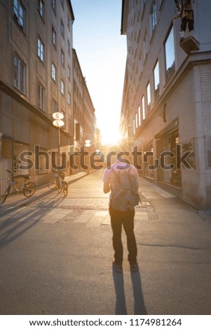 Young traveler with backpack  walking on street and looking  a map and using smart phone holding gadget which view from back of the tourist traveler in Europe.Sun flare in evening