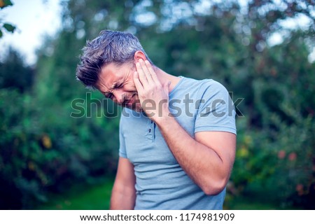 Unhappy man having ear pain touching his painful head outdoor Royalty-Free Stock Photo #1174981909
