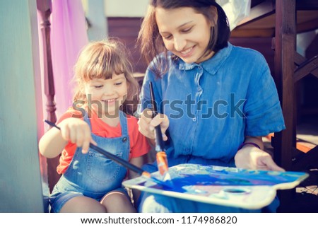 Beautiful smiling girl artists drawing a picture together, holding brush with blue paint and palette. Family hobby, art for children, art school
