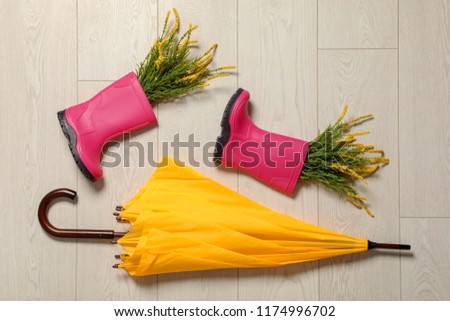 Flat lay composition with umbrella and rubber boots on wooden background