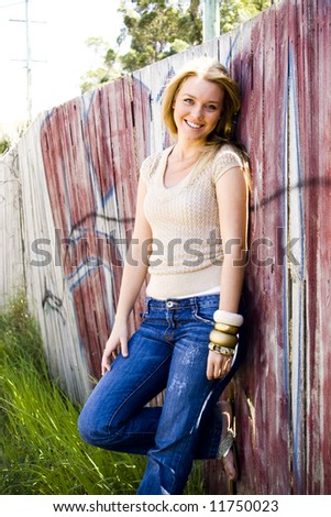 beautiful young girl standing in front of a graffiti fence